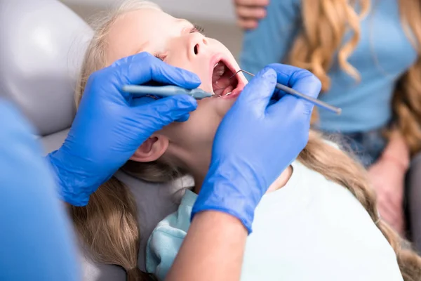Corte tiro de dentista fêmea examinando dentes de criança pequena, enquanto os pais sentados perto dela — Fotografia de Stock