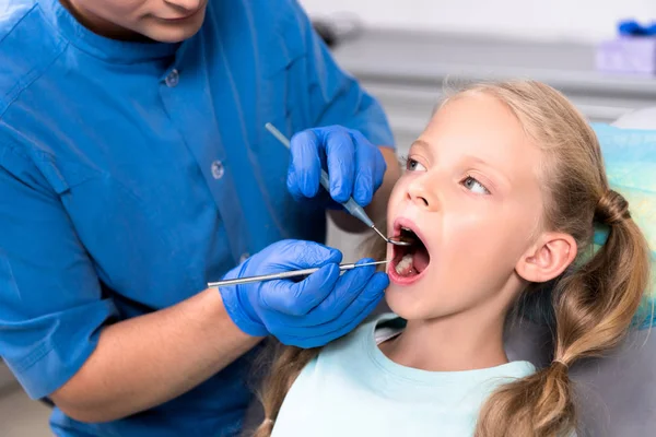 Recortado tiro de dentista con herramientas examinar los dientes de niño pequeño - foto de stock