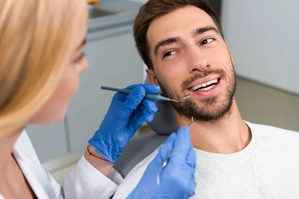 Крупним планом знімок жіночого стоматолога, який вивчає зуби молодого щасливого клієнта — Stock Photo