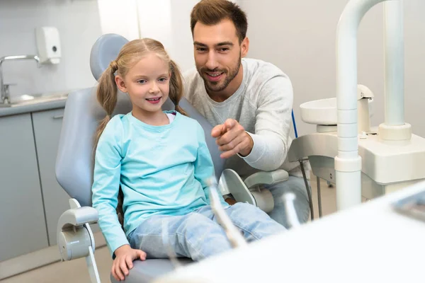 Father and daughter in dentist office looking at stand with tools — Stock Photo