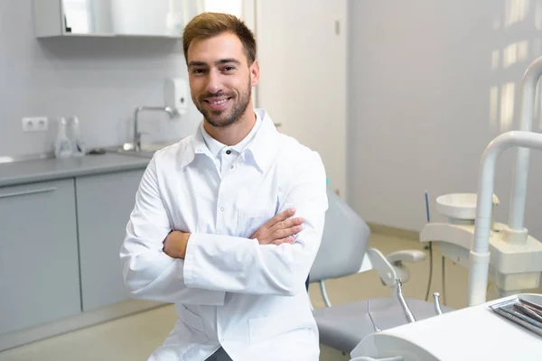 Glückliche junge Zahnärztin mit verschränkten Armen blickt in die Kamera im Büro — Stockfoto