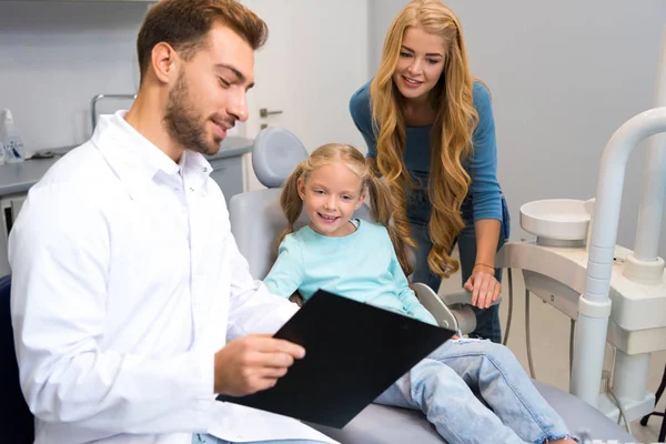 Dentist showing clipboard to mother and little daughter — Stock Photo