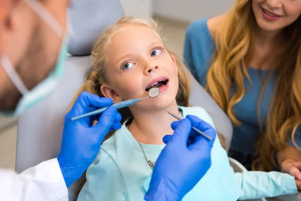 Cropped shot of dentist working with adorable little child while young mother sitting near her for support — Stock Photo