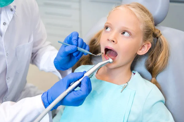 Recortado disparo de dentista examinando los dientes de hermoso niño - foto de stock