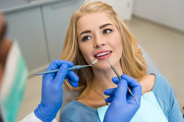 Tiro recortado de dentista examinando dentes de belo cliente feminino — Fotografia de Stock