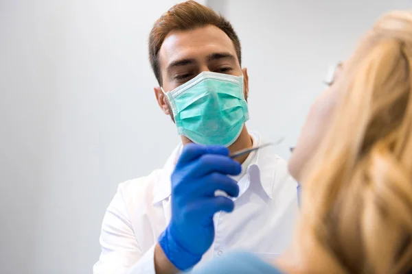 Vista inferior de joven dentista en máscara examinar los dientes de cliente femenino - foto de stock