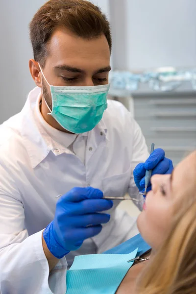 Joven dentista en máscara examinar los dientes de cliente femenino - foto de stock