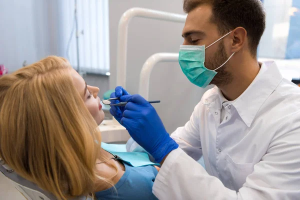 Bonito jovem dentista examinando dentes de cliente feminino — Fotografia de Stock