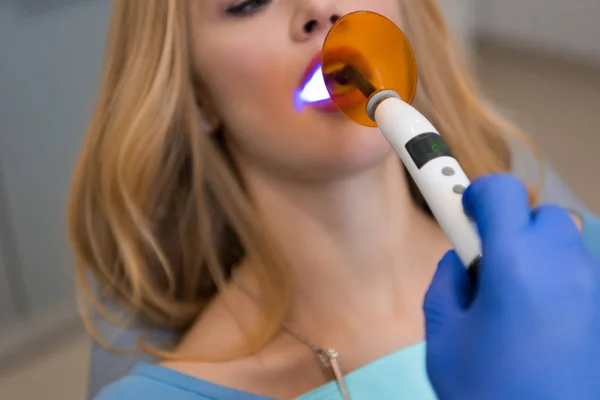 Cropped shot of dentist in glove making procedure with dental curing light for female client — Stock Photo