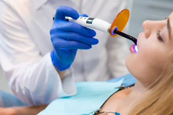 Plan recadré de dentiste en gant avec la lumière de durcissement dentaire travaillant avec le client féminin — Photo de stock