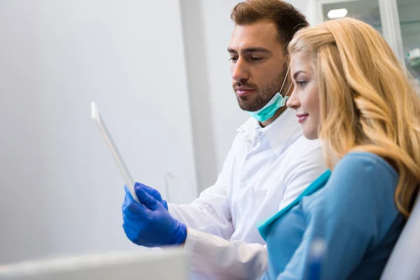 Bonito jovem dentista mostrando tablet para cliente do sexo feminino — Fotografia de Stock