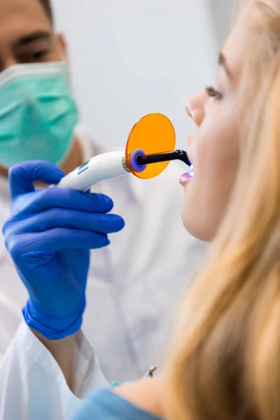 Young dentist with dental curing light working with female client — Stock Photo