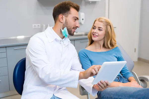 Attrayant jeune dentiste montrant comprimé à la cliente — Photo de stock