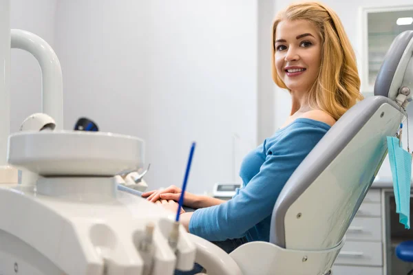 Mujer joven sonriente sentada en silla dental en el consultorio del dentista - foto de stock