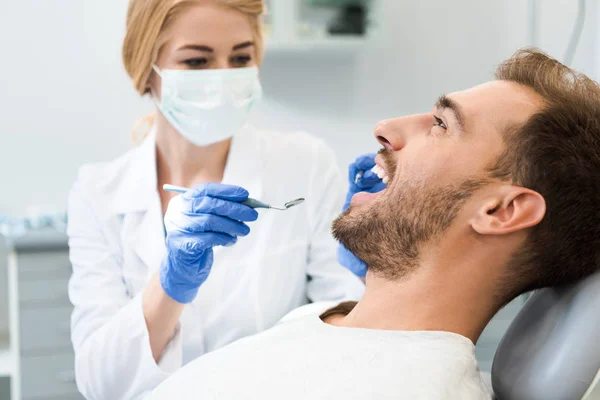 Giovane dentista donna esaminando i denti di bel cliente sorridente in sedia dentale — Foto stock