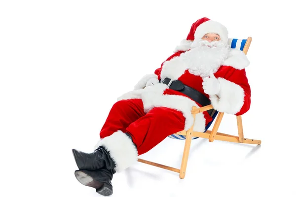 Санта Клаус показує великий палець вгору і розслабляється на пляжному кріслі на білому — стокове фото
