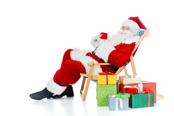 Santa Claus sosteniendo taza de café y sentado en la silla de playa con regalos de Navidad en blanco - foto de stock