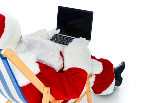 Santa claus using laptop with blank screen while resting on beach chair isolated on white — Stock Photo
