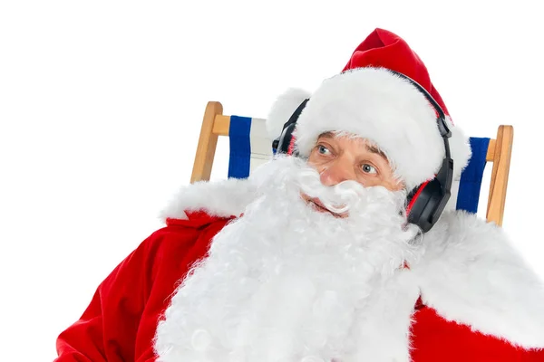 Babbo Natale ascoltare musica con le cuffie mentre seduto sulla sedia da spiaggia isolato su bianco — Foto stock