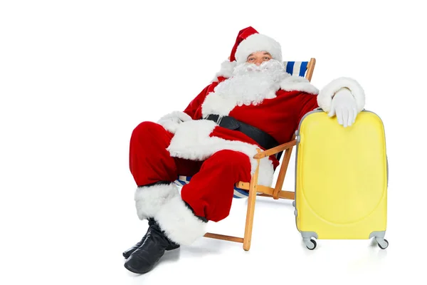 Santa claus barbu relaxant dans une chaise de plage avec sac de voyage jaune isolé sur blanc — Photo de stock