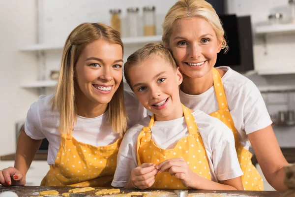 Adorable happy child with mother and grandmother smiling at camera together in kitchen — Stock Photo