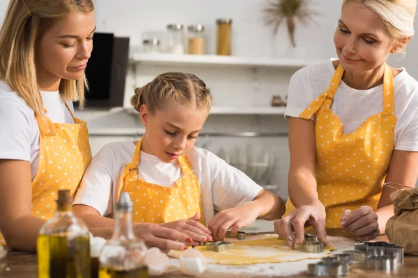 Família de três gerações em aventais preparando biscoitos juntos na cozinha — Fotografia de Stock
