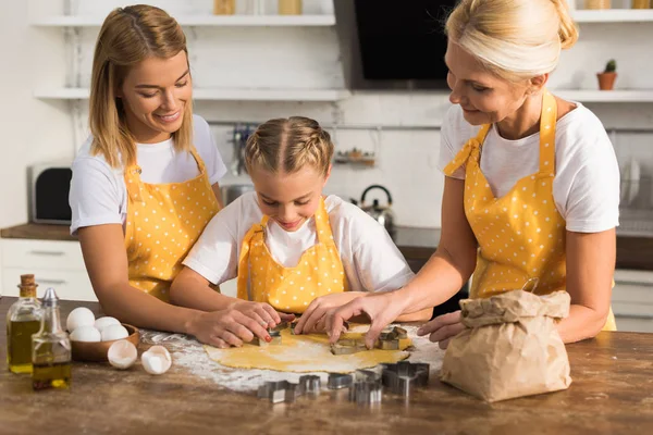 Niño feliz con la madre y la abuela preparando galletas juntos en la cocina - foto de stock