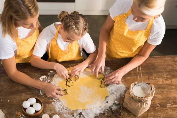 Overhead view of child with mother and grandmother preparing cookies together in kitchen — Stock Photo