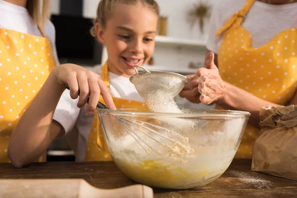 Обрезанный снимок улыбающегося ребенка с матерью и бабушкой, готовящих тесто вместе — стоковое фото