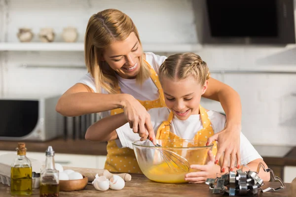 Mãe feliz e filha batendo ovos enquanto cozinham juntos — Fotografia de Stock
