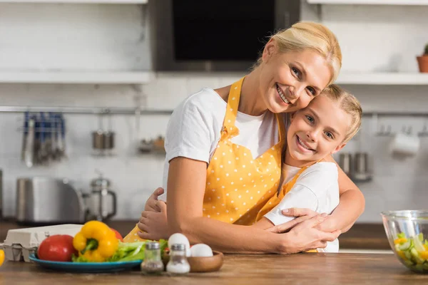 Glückliche Großmutter und Enkelin in Schürzen, die sich beim gemeinsamen Kochen umarmen und in die Kamera lächeln — Stockfoto