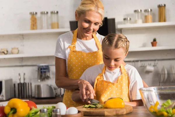 Glückliche Großmutter mit entzückender Enkelin beim gemeinsamen Kochen von Gemüsesalat in der Küche — Stockfoto