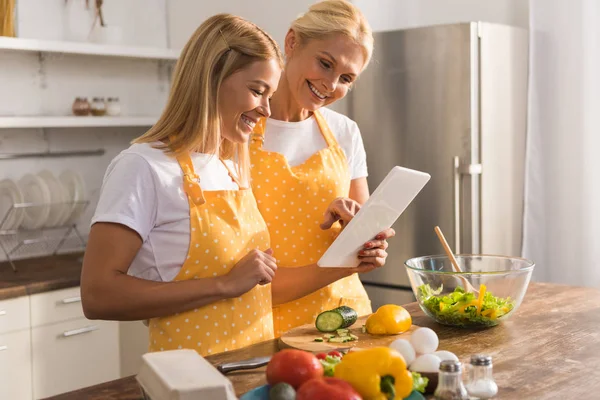 Счастливая взрослая мать и дочь с помощью цифрового планшета во время приготовления пищи вместе — стоковое фото
