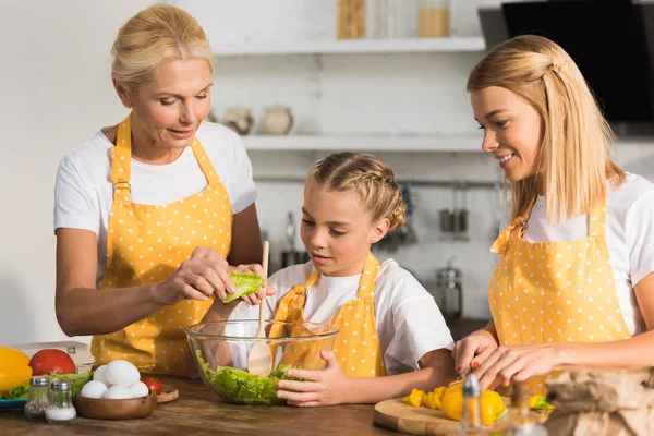 Entzückendes Kind mit Mutter und Großmutter beim Kochen von Gemüsesalat in der Küche — Stockfoto