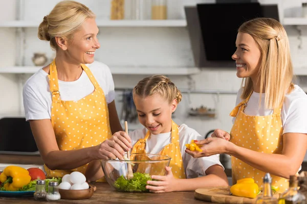 Feliz familia de tres generaciones cocinar ensalada de verduras juntos - foto de stock