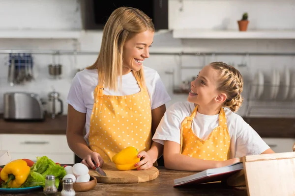 Hermosa feliz madre e hija sonriendo el uno al otro y cocinar juntos - foto de stock