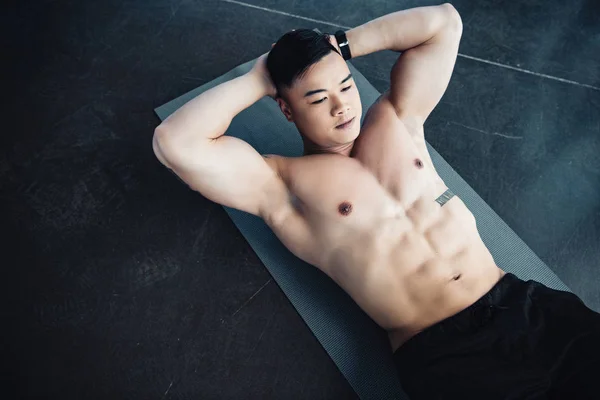 Joven asiático deportista con desnudo pecho haciendo abs ejercicio en fitness mat en gimnasio - foto de stock