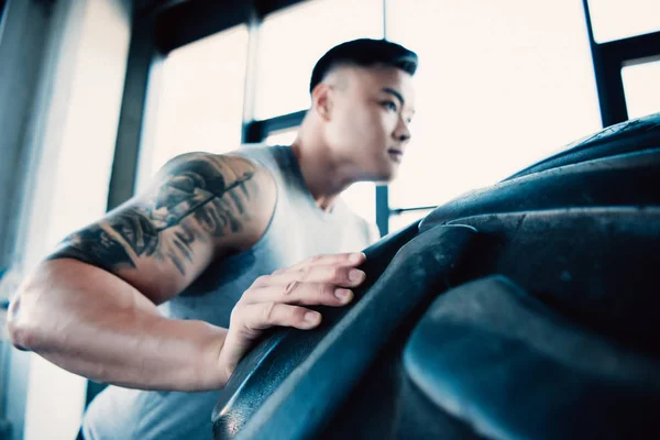 Concentrated young sportsman flipping heavy tire at gym — Stock Photo