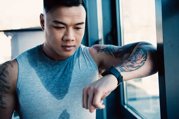 Young sweaty tired asian sportsman after long workout looking at watch — Stock Photo