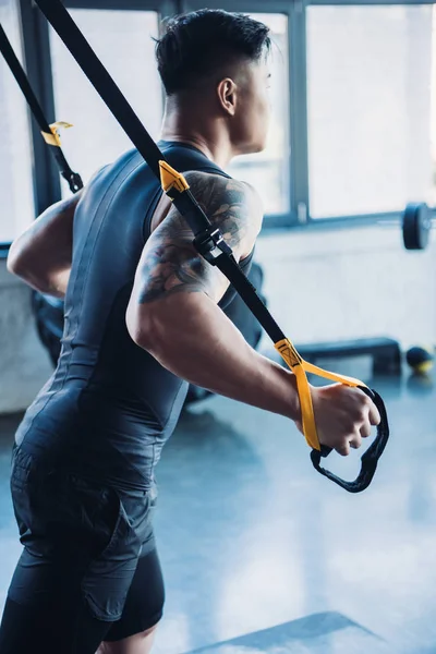Side view of young muscular sportsman training with resistance bands in gym — Stock Photo