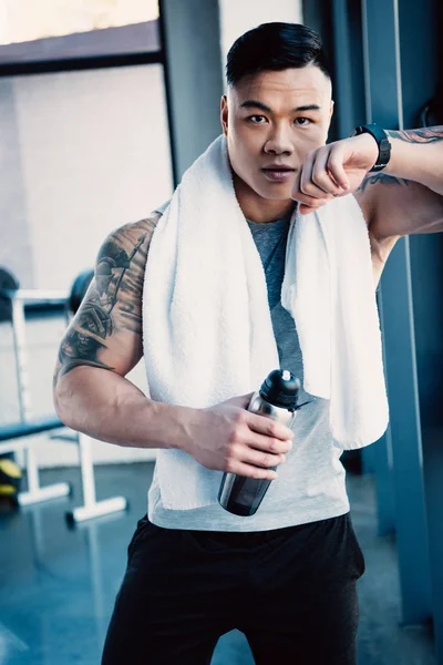 Young tired sportsman with towel and bottle of water after long workout — Stock Photo