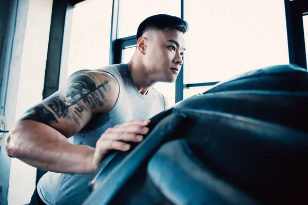 Handsome young sportsman flipping heavy tire at gym — Stock Photo