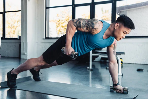 Giovane sportivo concentrato che si allena con i manubri in palestra sul tappeto sportivo — Foto stock