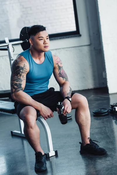 Schöner junger Sportler sitzt mit Wasserflasche im Fitnessstudio — Stockfoto