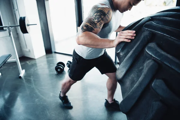 Cropped view of young sportsman flipping heavy tire at gym — Stock Photo