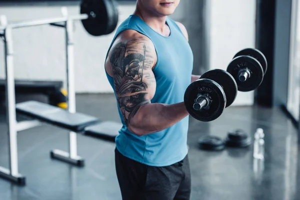 Vista parcial del joven deportista haciendo ejercicio con pesas en el gimnasio - foto de stock