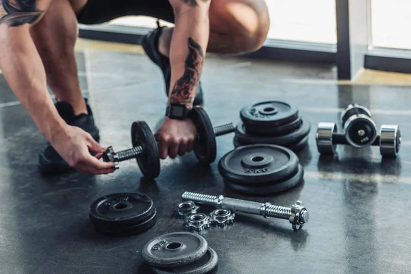 Partial view of tattooed sportsman assembling dumbbells — Stock Photo