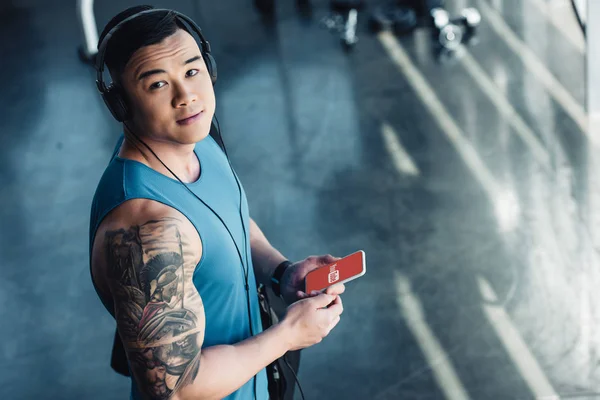 Молодой азиатский спортсмен, использующий смартфон и слушающий музыку — стоковое фото