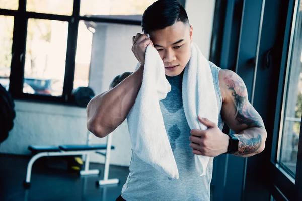 Молодой азиатский спортсмен вытирает лицо полотенцем после долгой тренировки — стоковое фото