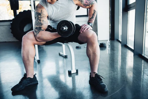 Vue partielle du jeune sportif faisant de l'exercice avec haltère dans la salle de gym — Photo de stock